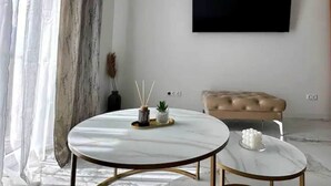 Een moderne woonkamer met een ronde marmeren salontafel, een beige bank en een flatscreen televisie aan de muur bevestigd.