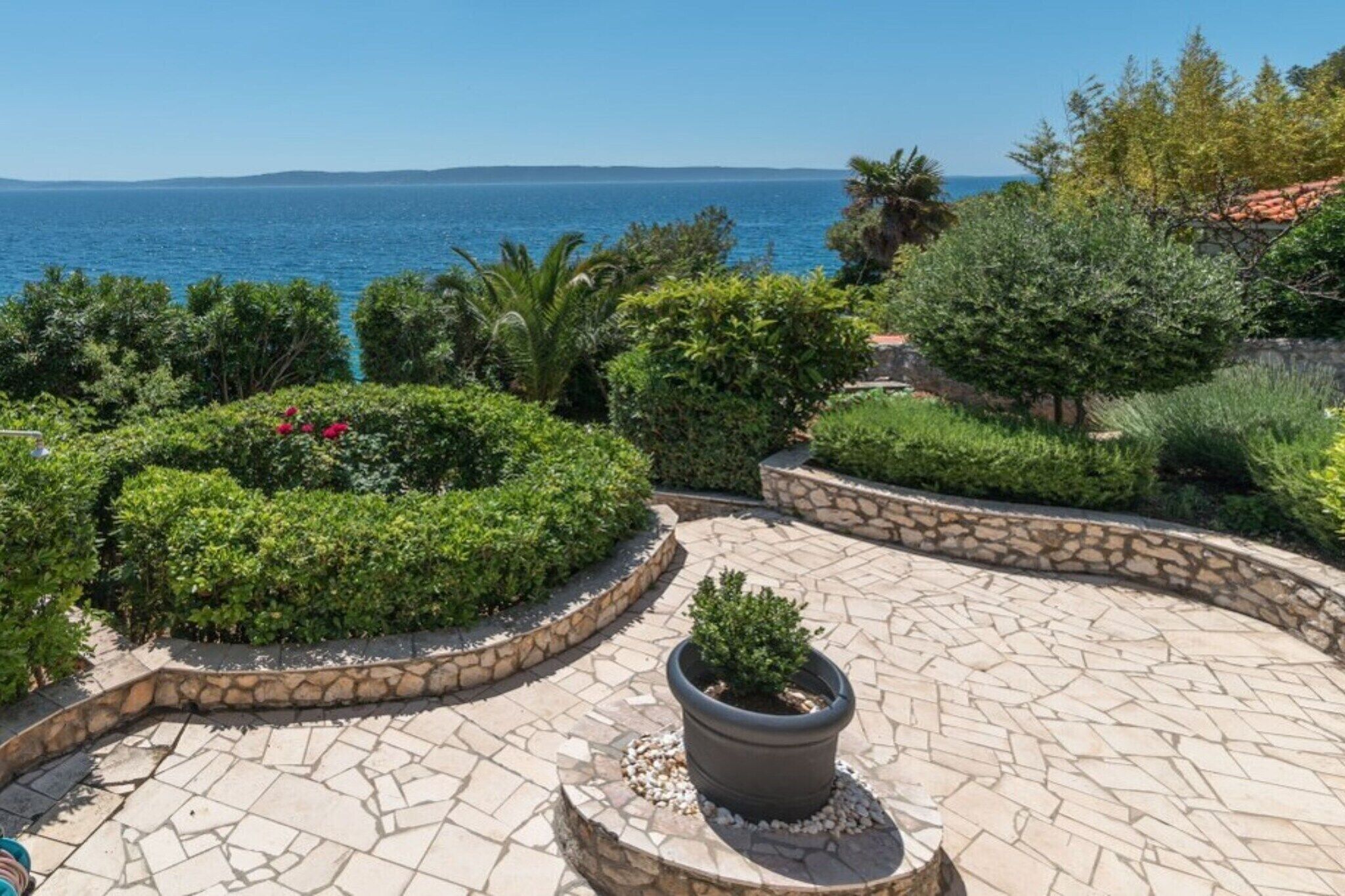 A landscaped outdoor area with a stone pathway, potted plants, and a view of the sea.