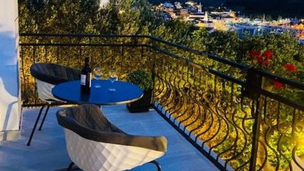 Ein Balkon mit zwei Stühlen und einem Tisch, mit Blick auf einen Weinberg und eine Stadt.