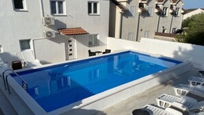 Ein rechteckiger Pool mit klar blauem Wasser, umgeben von weißen Liegestühlen und einem kleinen Tisch.