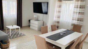 Ein modernes Hotelzimmer mit Essbereich, einem flachbildfernseher an der Wand, einem kleinen weißen Tisch und einem Esstisch mit Stühlen.
