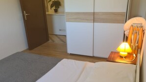 A hotel room with a bed, a bedside lamp, a wardrobe, and a small table with a lamp. - Apartments Rubbi - Three Bedroom Apartment with Terrace (Vrsi)