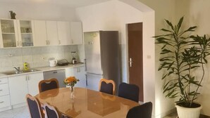 A dining area with a wooden table and chairs, a potted plant, and a kitchen with white cabinets and appliances. - Apartments Rubbi - Three Bedroom Apartment with Terrace (Vrsi)