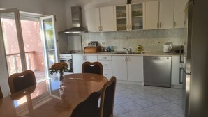 A modern kitchen with white cabinets, a stainless steel dishwasher, and a dining area with a glass table and chairs. - Apartments Rubbi - Three Bedroom Apartment with Terrace (Vrsi)