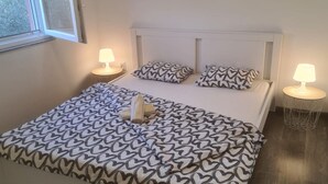 A neatly made bed with patterned bedding, two bedside lamps, and a window with a view of trees. - Apartments Rubbi - Two Bedroom Apartment with Terrace (Vrsi)