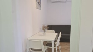 A dining area with a white table and chairs, a vase with dried flowers, and a dark-colored sofa in the background. - Apartments Rubbi - Two Bedroom Apartment with Terrace (Vrsi)
