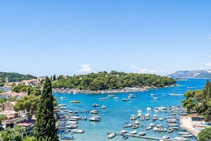 A coastal town with numerous boats docked along the waterfront, surrounded by lush greenery and a clear blue sky.