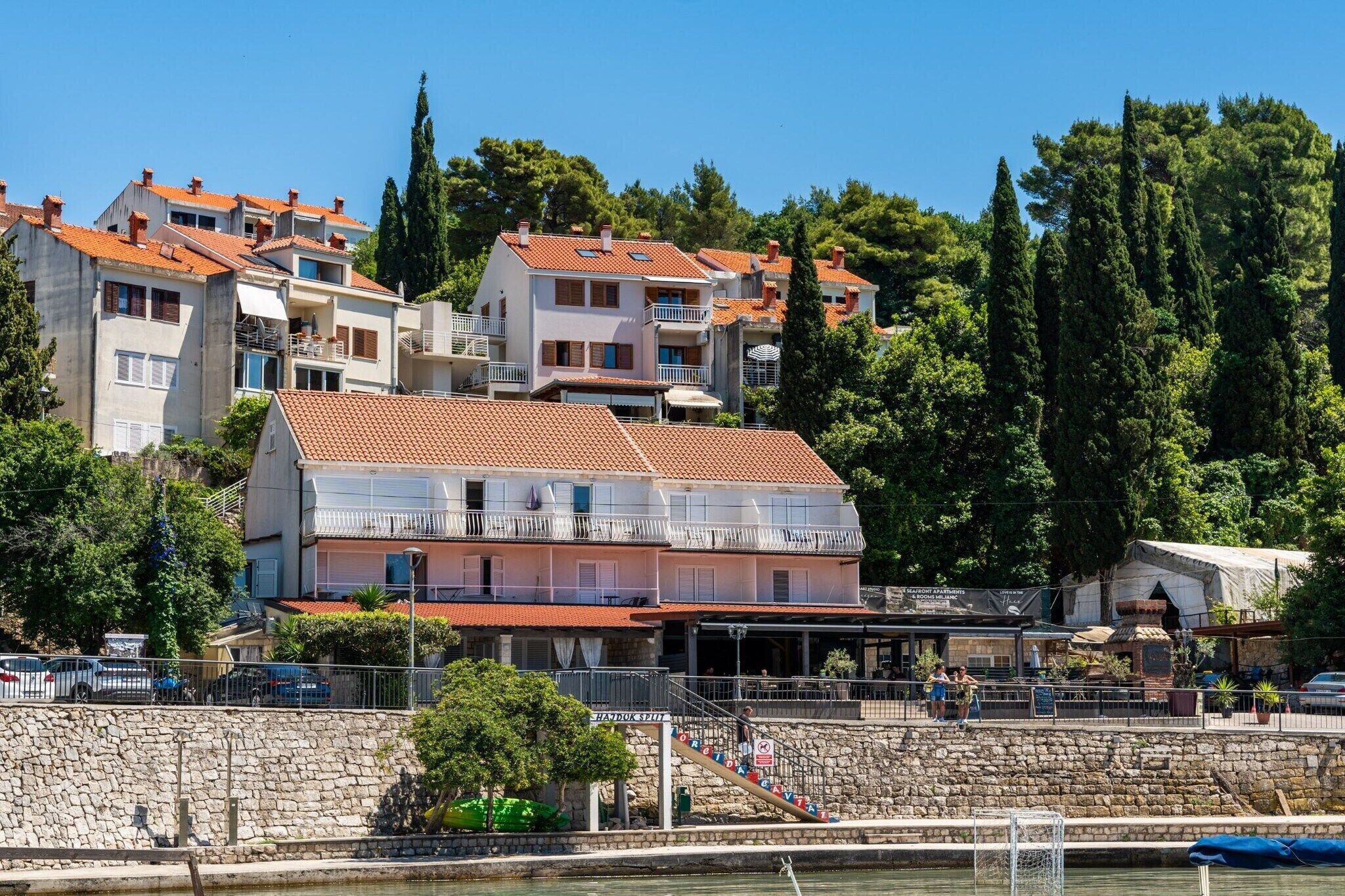 Un edificio sul lungomare con diversi balconi, un muro in pietra e una vista libera sul mare.