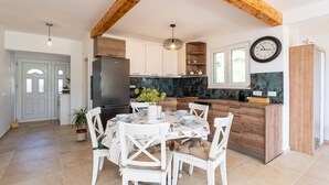 A modern kitchen with wooden beams, a marble countertop, and a dining area with white chairs and a table set for four.