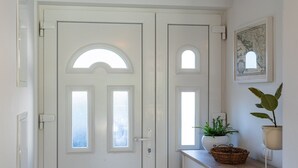 A white door with a semi-circular window and a smaller rectangular window, flanked by a wall-mounted map and a potted plant.