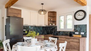A modern kitchen with a built-in refrigerator, wooden cabinets, a marble backsplash, and a dining area with white chairs and a table set for four.
