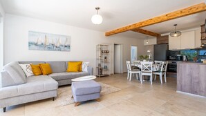 A modern living room with a grey sofa, ottoman, and dining area with white chairs and a wooden table.