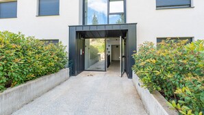 Une entrée moderne, avec une porte en verre et un chemin en béton bordé de verdure.