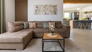 A modern living room with a sectional sofa, a coffee table, and a kitchen in the background. - Holiday Home Milevoj - Three Bedroom Holiday Home (Labin)