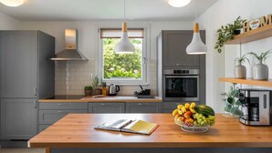 A modern kitchen with grey cabinets, a wooden countertop, a window with a view of greenery, a coffee machine, and a fruit bowl. - Holiday Home Milevoj - Three Bedroom Holiday Home (Labin)