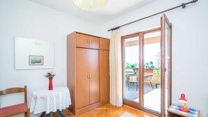 A room with a wooden wardrobe, a table with a vase of flowers, a chair, and a view through a glass door to an outdoor area with a table and chairs. - Comfortable Kastel Stafilic Apartment with Balcony - Two Bedroom Apartment with Balcony and Sea View (Kastel Stafilic)