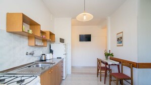 A compact kitchen with a gas stove, a sink, wooden shelves, and a dining area with a table and chairs. - Comfortable Kastel Stafilic Apartment with Balcony - Two Bedroom Apartment with Balcony and Sea View (Kastel Stafilic)