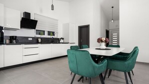 Eine moderne Küche mit weißen Schränken, einer schwarzen Arbeitsplatte und einem Essbereich mit weißem Tisch und grünen Stühlen.