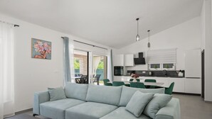 Ein modernes Wohnzimmer mit einem hellgrünen Sofa, einem Essbereich mit grünen Stühlen und einer Küche mit weißen Schränken und einer schwarzen Arbeitsplatte.