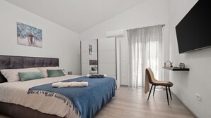 Ein modernes Schlafzimmer mit Bett, Sessel, Fernseher und Regal.