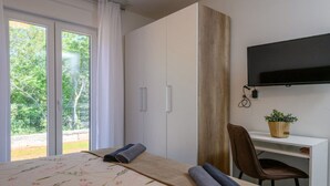 A bedroom with a bed, a desk, a chair, a TV, and a sliding door to a balcony. - Three Bedroom Villa with Swiming Pool (Rasa)