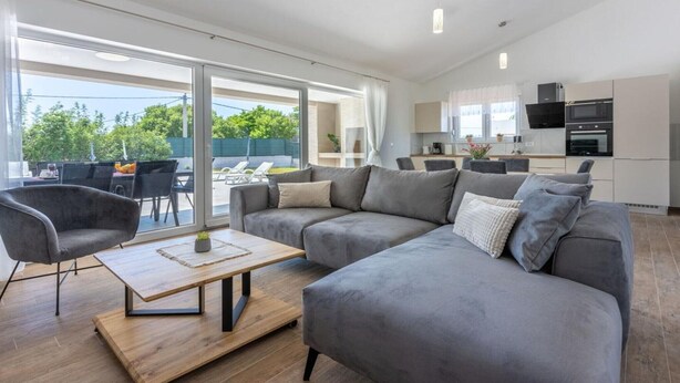 A modern living room with a grey sofa, a wooden coffee table, and a dining area with chairs and a table. - Three Bedroom Villa with Swiming Pool (Rasa)