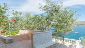 Una terraza costera con barandilla de piedra, vista despejada del mar y una farola.