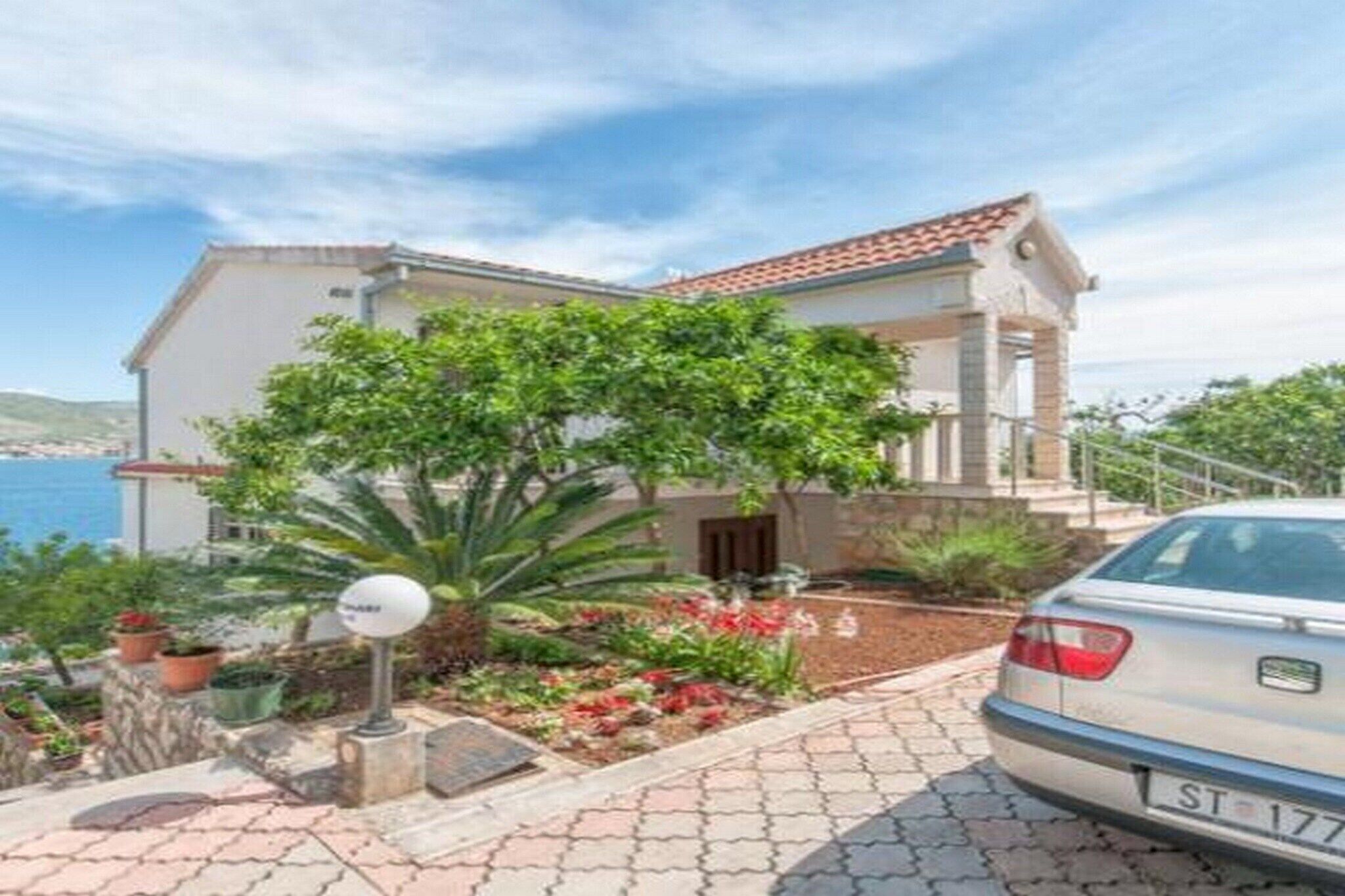 A two-story building with a tiled roof, a garden with various plants and flowers, and a parked car.