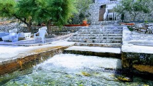 Una escalera de piedra conduce a una zona de piscina con agua cristalina, rodeada de árboles y mobiliario exterior.