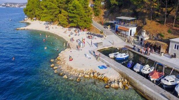 Una zona costera con playa, agua cristalina y barcos amarrados a la orilla.