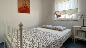 Une chambre à coucher avec un lit, une table de chevet, une fenêtre avec des rideaux et un tableau au mur.