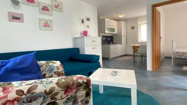 Un salon moderne avec un canapé bleu, une table basse blanche et un coin cuisine à l’arrière-plan.