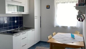 Une cuisine compacte avec des meubles blancs, un plan de travail bleu carrelé, un évier en acier inoxydable et une table à manger avec des chaises.
