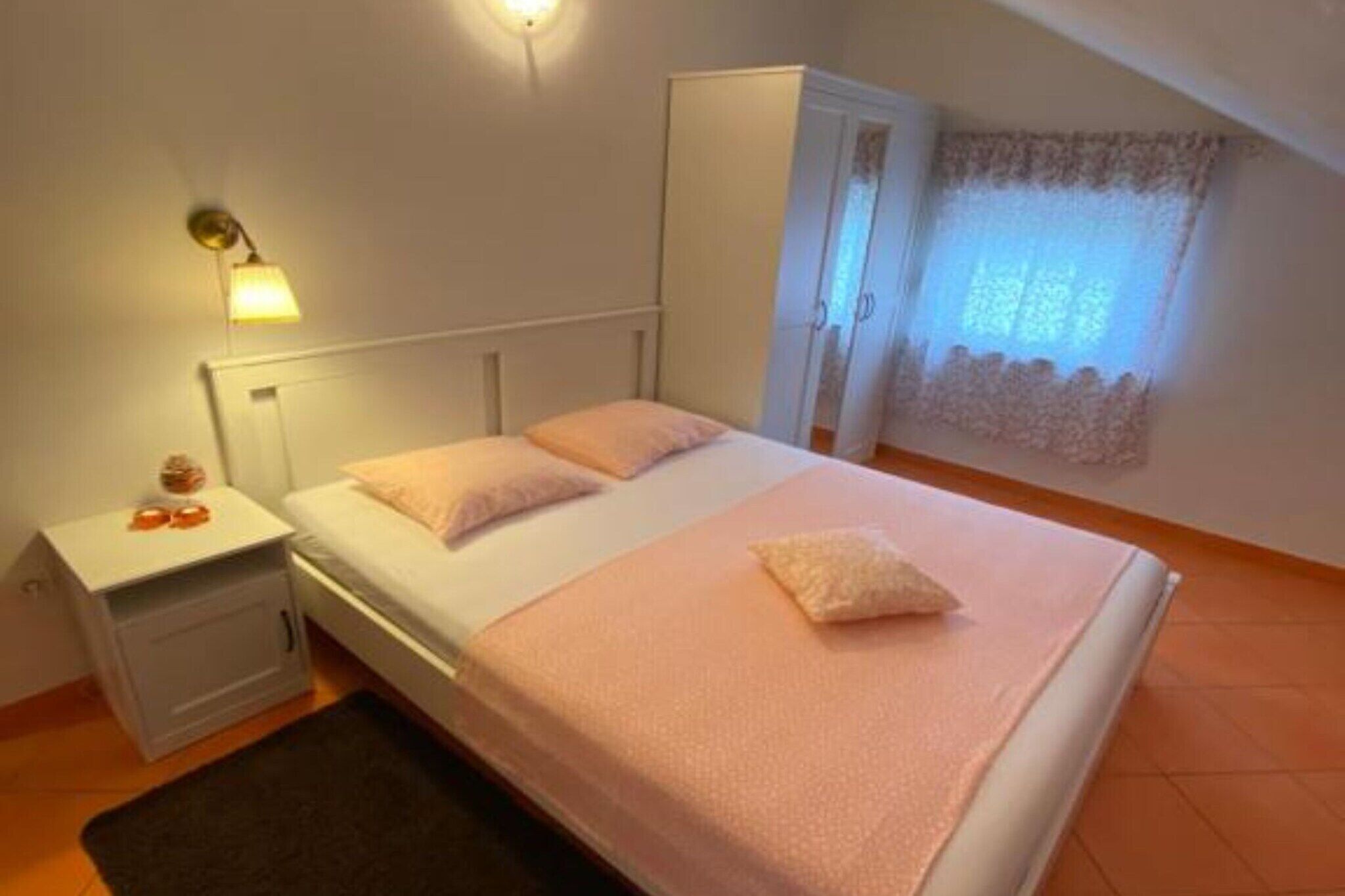 A bedroom with a bed, nightstand, wardrobe, and a window with curtains.
