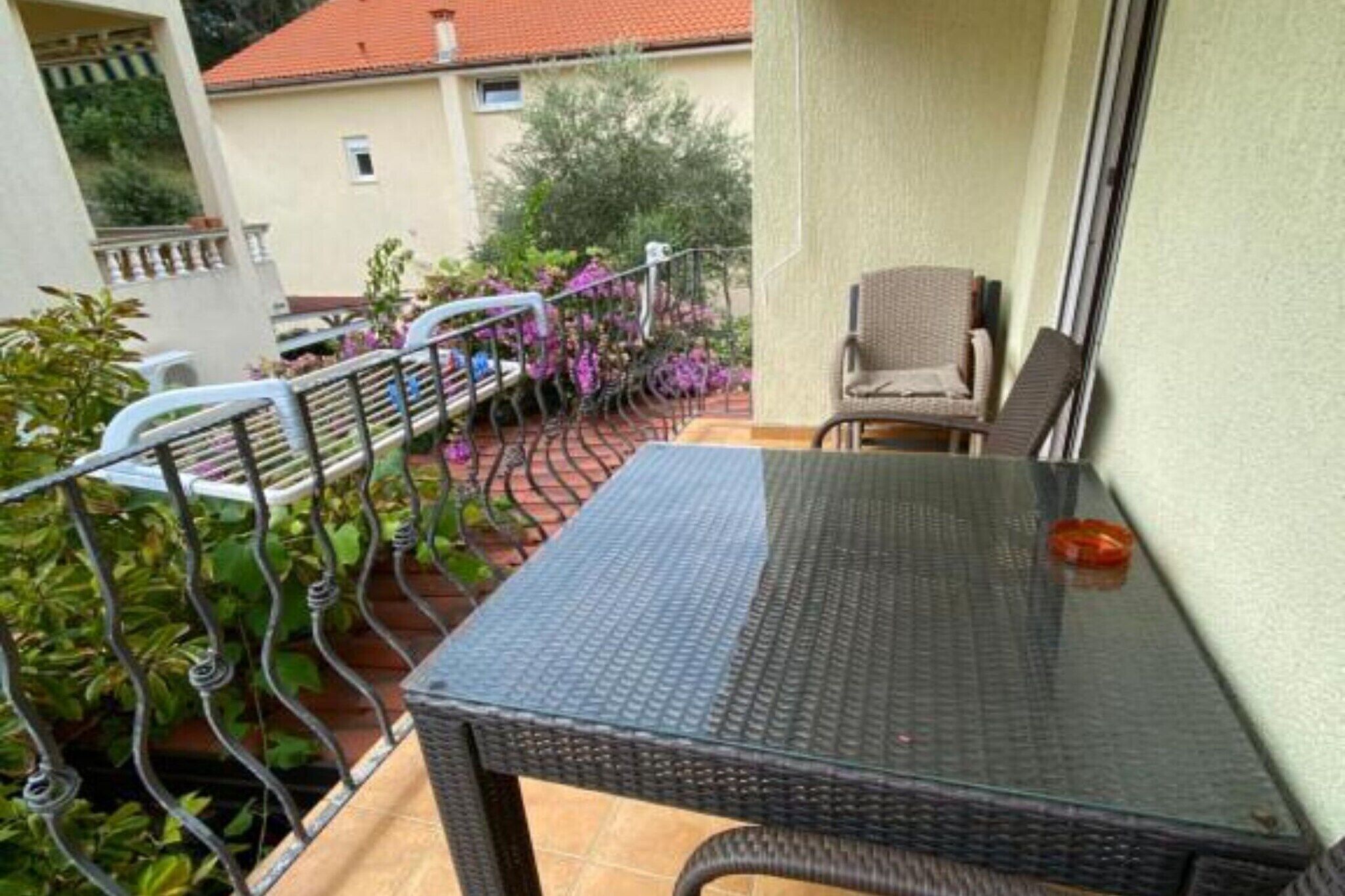 A balcony with a glass table, wicker chairs, and a metal railing.