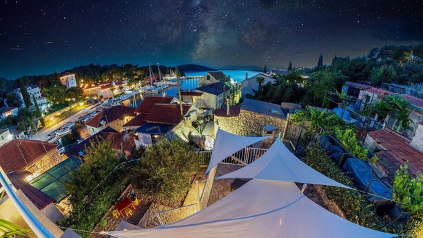 A coastal town at night with a starry sky, boats docked along the waterfront, and buildings with red roofs. - Holiday Home Lea - Three Bedroom Holiday Home with Terrace and Sea View (Maslinica)