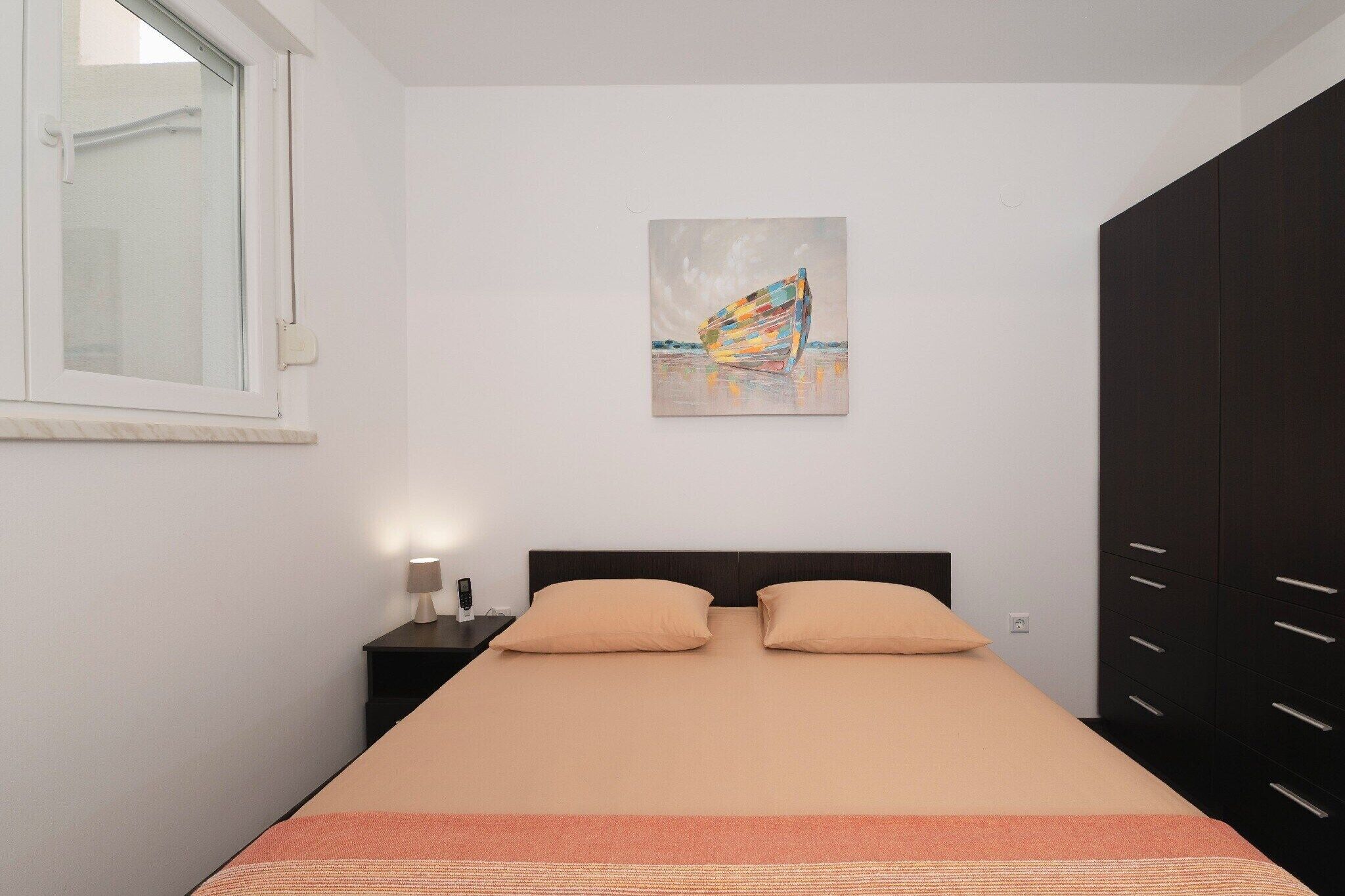 Un dormitorio con cama, mesita de noche, lámpara, un cuadro y un armario.