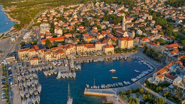 Vista aérea de una ciudad costera con un puerto deportivo lleno de barcos, rodeada de edificios residenciales y una iglesia destacada.