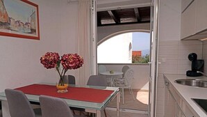 Un comedor con mesa y sillas, un florero con flores y vistas al balcón exterior a través de un puerta abierta.