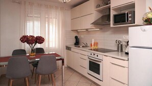 Una cocina moderna con armarios blancos, microondas, horno y refrigerador. Hay una mesa de comedor con sillas y un florero con flores.