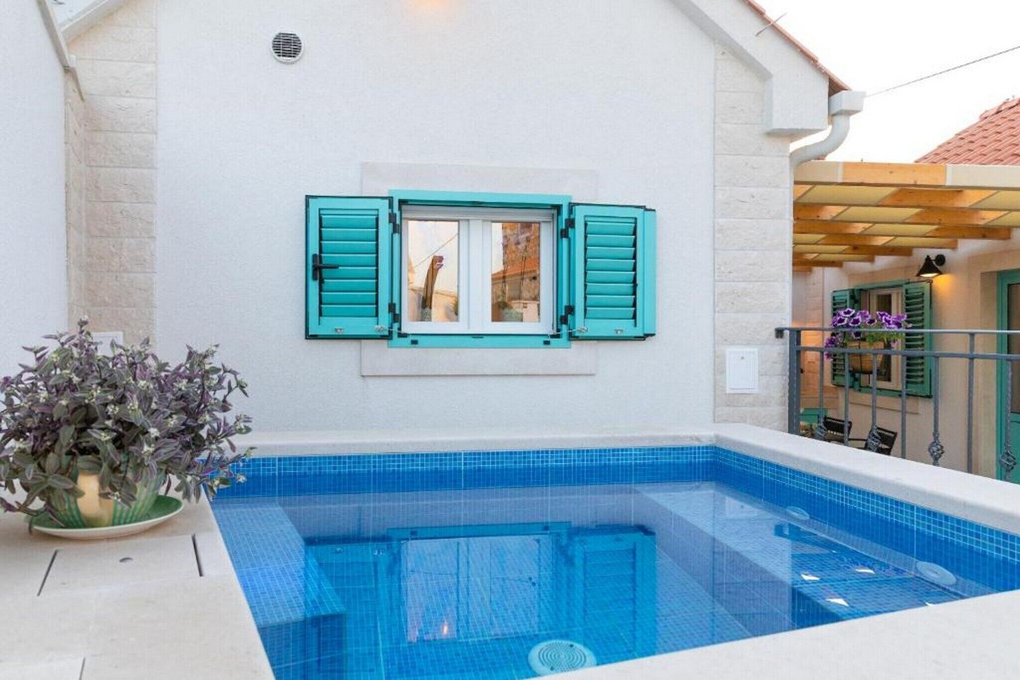 Una piscina con vista a un edificio con contraventanas color turquesa y una planta en maceta.