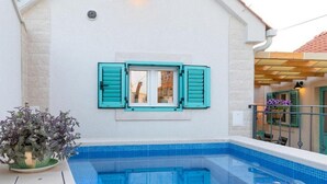 Ein Swimmingpool mit Blick auf ein Gebäude mit türkisblauen Fensterläden und einem Blumentopf.
