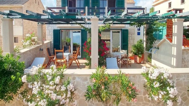 A two-story house with a covered patio area, outdoor furniture, and potted plants. - Apartments Gracin - One Bedroom Apartment with Terrace (A1) (Povlja)