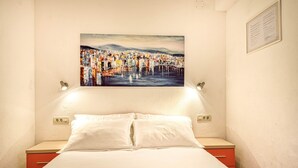 A hotel room with a bed, a red nightstand, a white pillow, a painting of a cityscape, and a wall-mounted light fixture. - Apartments Gracin - One Bedroom Apartment with Terrace (A1) (Povlja)
