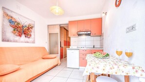A compact living space with a sofa, a dining table with a floral tablecloth, and a kitchen area with orange cabinets. - Apartments Gracin - One Bedroom Apartment with Terrace (A1) (Povlja)
