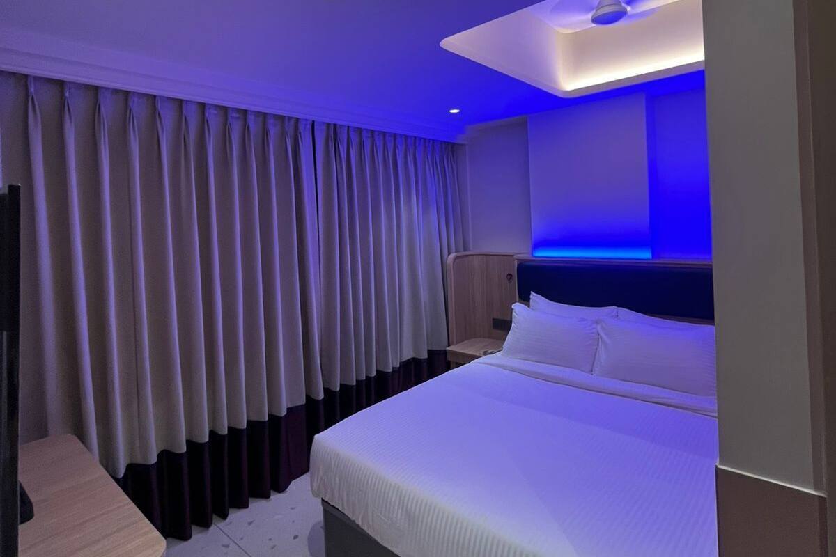 A modern hotel room with a large bed, a desk, and a ceiling light.