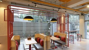 A modern cafe with high tables and cushioned seating, large windows, and red accents.