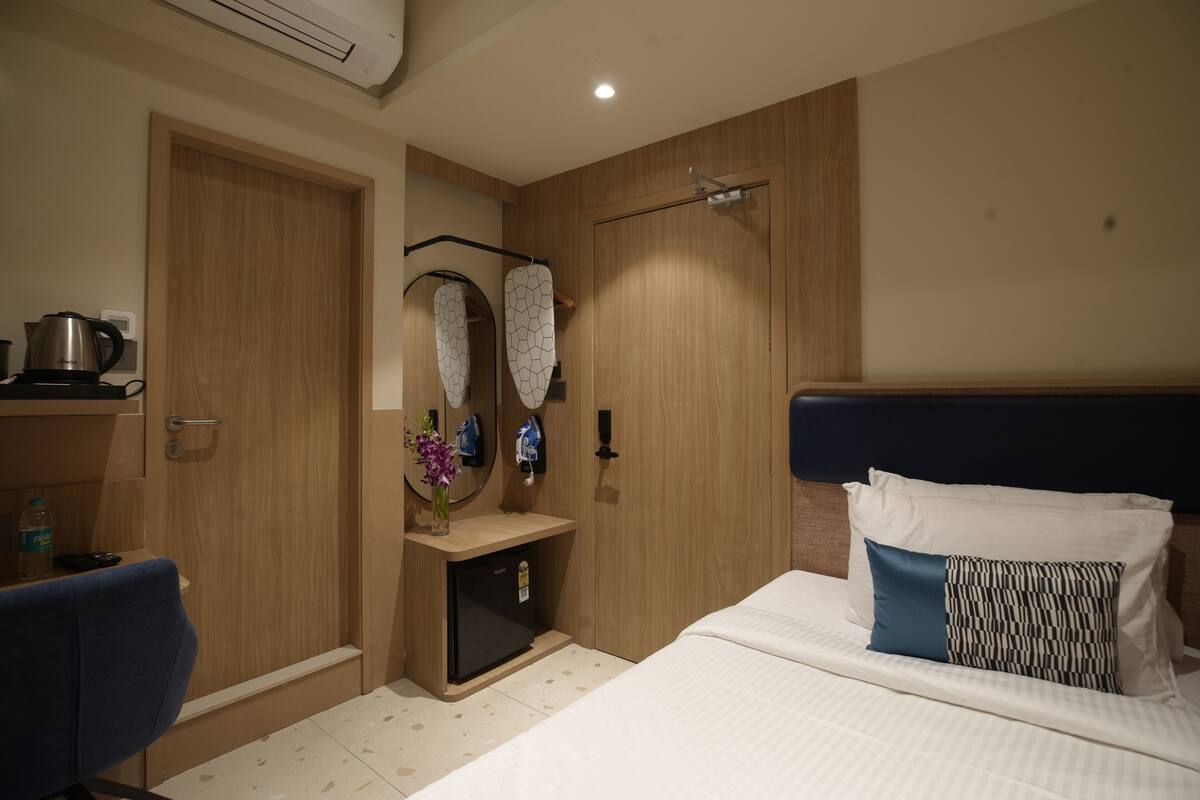 A hotel room with a bed, a desk with a chair, a small refrigerator, and a mirror.