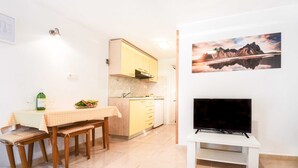 A compact kitchen with a dining area, a TV, and a painting on the wall.