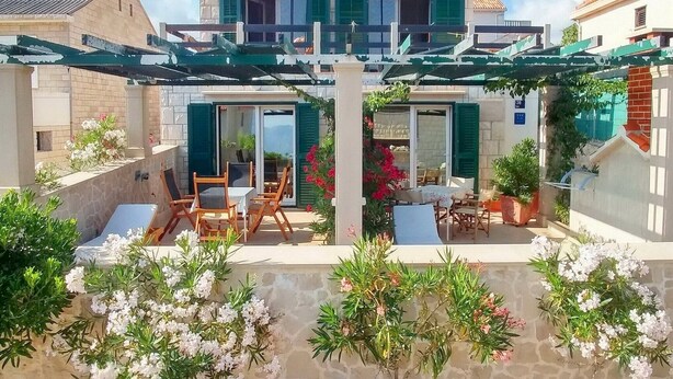 A two-story house with a covered patio area featuring outdoor seating and potted plants.